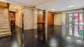 Un hall d’entrée spacieux avec un sol noir poli, un comptoir d’accueil en bois et un escalier situé sur la gauche.