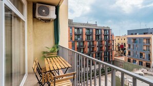 Un balcon avec une table et des chaises, un appareil de climatisation et une vue sur les bâtiments voisins.