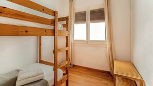 A small, single-room accommodation with a wooden bunk bed, a small table, and a window with curtains.
