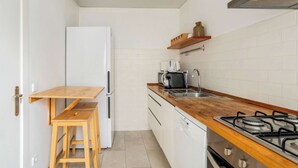 A compact kitchen with a white refrigerator, wooden stools, a gas stove, and a coffee maker.