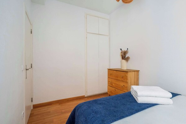 A bedroom with a wooden dresser, a bed with a blue blanket, and a white door.