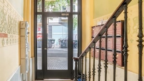 Ein Flur mit einer Tür, die zu einem Außenbereich führt, einer Treppe mit einem Holnlaufgeländer und Wandverzierungen mit Muster.