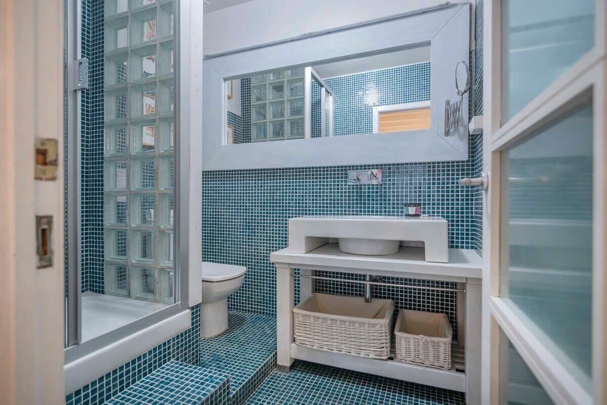 Un baño con inodoro, lavabo y espejo. Hay una ventana con diseño de cuadrícula y una puerta.