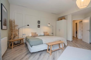 Une chambre à coucher avec un grand lit, des tables de chevet, un banc et une lampe suspendue.