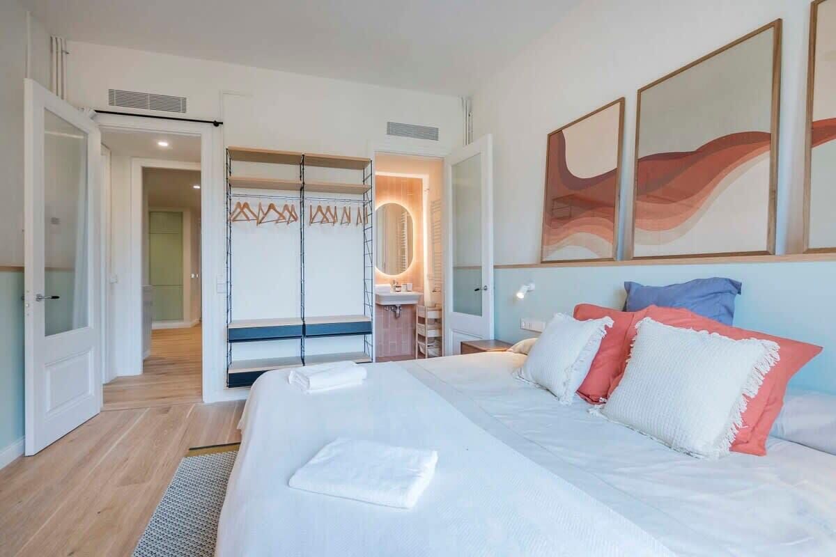 A hotel room with a large bed, a bathroom with a mirror, and a door leading to another room.