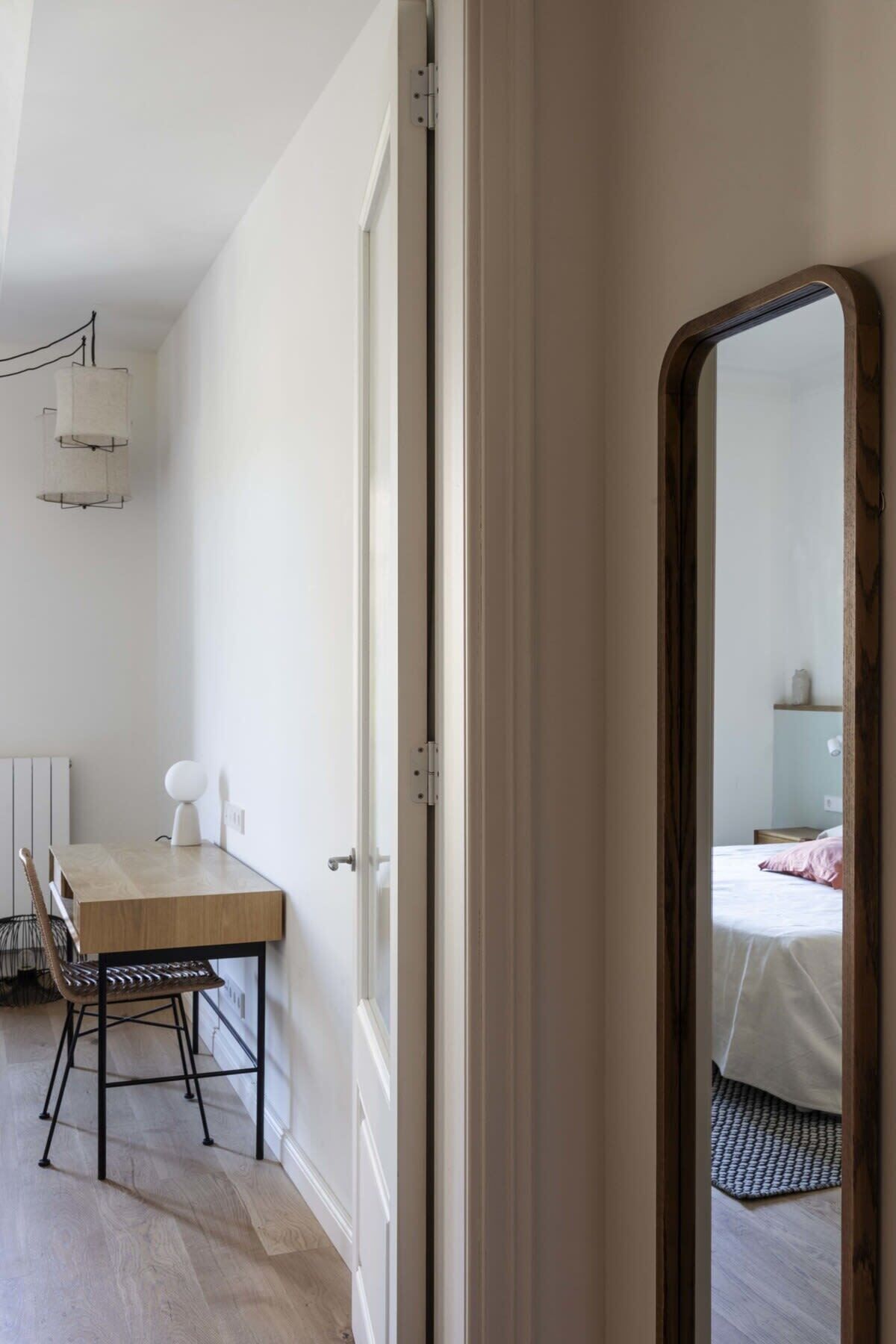 A room with a wooden dining table, chairs, a white radiator, and a bed with a pink pillow.