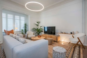 A modern living room with a sofa, chairs, a TV, and decorative plants.