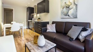 Ein modernes Wohnzimmer mit einem dunkelbraunen Sofa, weißen und gemusterten Kissen, einem Holztisch und einem Bild von Vasen an der Wand.