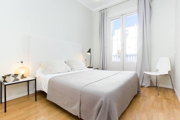 Une chambre à coucher au style minimaliste, avec un grand lit, des tables de chevet, une chaise et une fenêtre avec des rideaux.