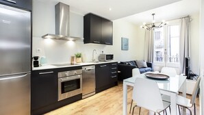 A modern kitchen with stainless steel appliances, black cabinetry, and a dining area with white chairs. - Centric 2bedroom in Las Ramblas (Barcelona)