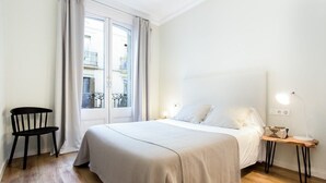A bedroom with a bed, a chair, a bedside table with a lamp, and a window with curtains. - Centric 2bedroom in Las Ramblas (Barcelona)