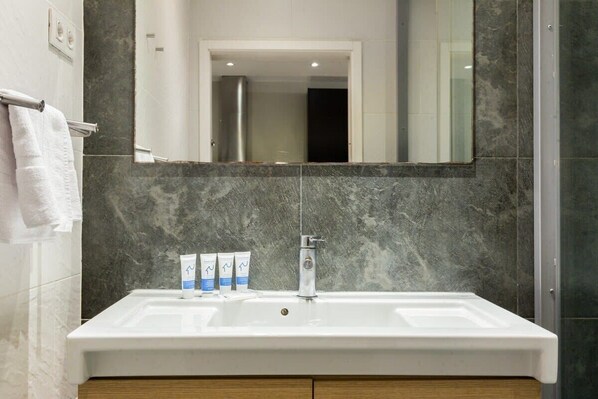 A bathroom with a white sink, a mirror, and a shower area. - The Collection - Centric 3bedroom in Las Ramblas (Barcelona)