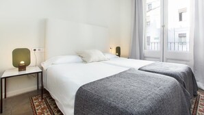 A hotel room with a bed, two bedside tables, a lamp, and a view of buildings through the window.