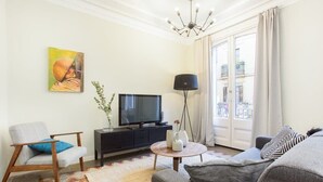 A living room with a sofa, armchair, TV, and a painting on the wall.