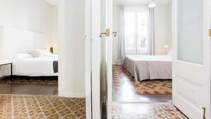 A hotel room with a bed, a nightstand, a lamp, and a view of the street through a window.