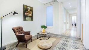 A living room with a brown leather armchair, a small table with a plant, a floor lamp, and a painting on the wall.