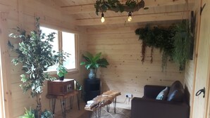 Ein gemütliches Zimmer mit Holzwänden, einem schwarzen Ledersofa, einem Holztisch und mehreren Blumentöpfen.