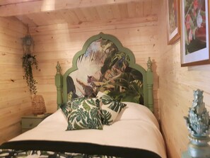 A wooden-paneled room with a bed featuring a green headboard and tropical-themed pillows. - Cabin set in a Beautiful Romantic Tropical Garden (Sutton Coldfield)