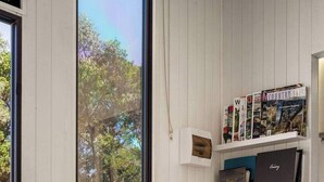 Een knus kamertje met een houten tafel en twee stoelen, een boekenkast met verschillende boeken en een 'Guest Book', en een raam met uitzicht op bomen.