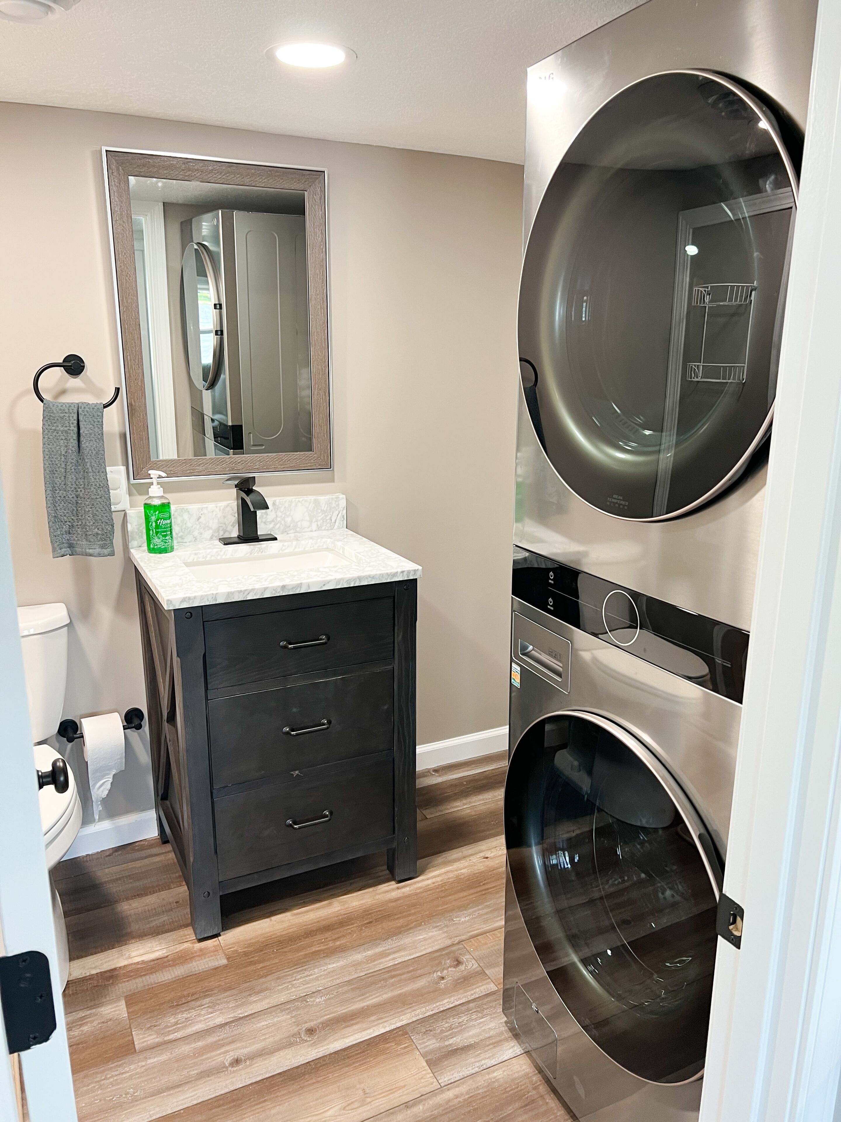 Un baño moderno con lavamanos de mármol, tocador de madera oscura, un espejo grande, inodoro y lavadora y secadora integradas.