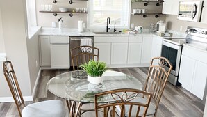 A modern kitchen with white cabinets, a glass dining table, and wooden chairs.
