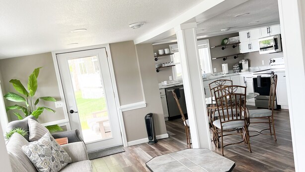A modern living room with a grey sofa, a coffee table, and a dining area with wicker chairs.
