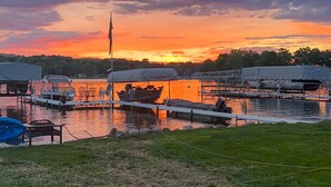 A marina with boats docked, a grassy area in the foreground, and a sunset in the background.