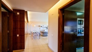A hallway leading to a dining area with a table and chairs, a sofa, and an oven in the kitchen. - FLH Salgados Family Apartment (Albufeira)