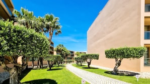 A courtyard with a cobblestone path, palm trees, and a building with a beige exterior. - FLH Salgados Family Apartment (Albufeira)