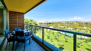 A balcony with a table and chairs, overlooking a well-maintained garden and a distant view of buildings. - FLH Salgados Family Apartment (Albufeira)
