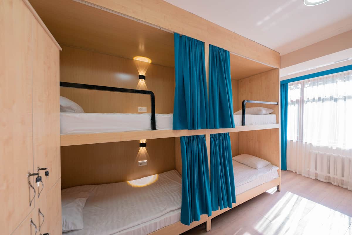 A bunk bed room with a wooden ceiling, a window with curtains, and a wall-mounted light fixture.