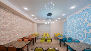 A conference room with multiple tables and chairs, a brick wall, and a blue patterned wall. - Hostel Kaganat (Bishkek)