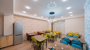 A dining area with multiple tables and chairs, a refrigerator, and a brick wall. - Hostel Kaganat (Bishkek)