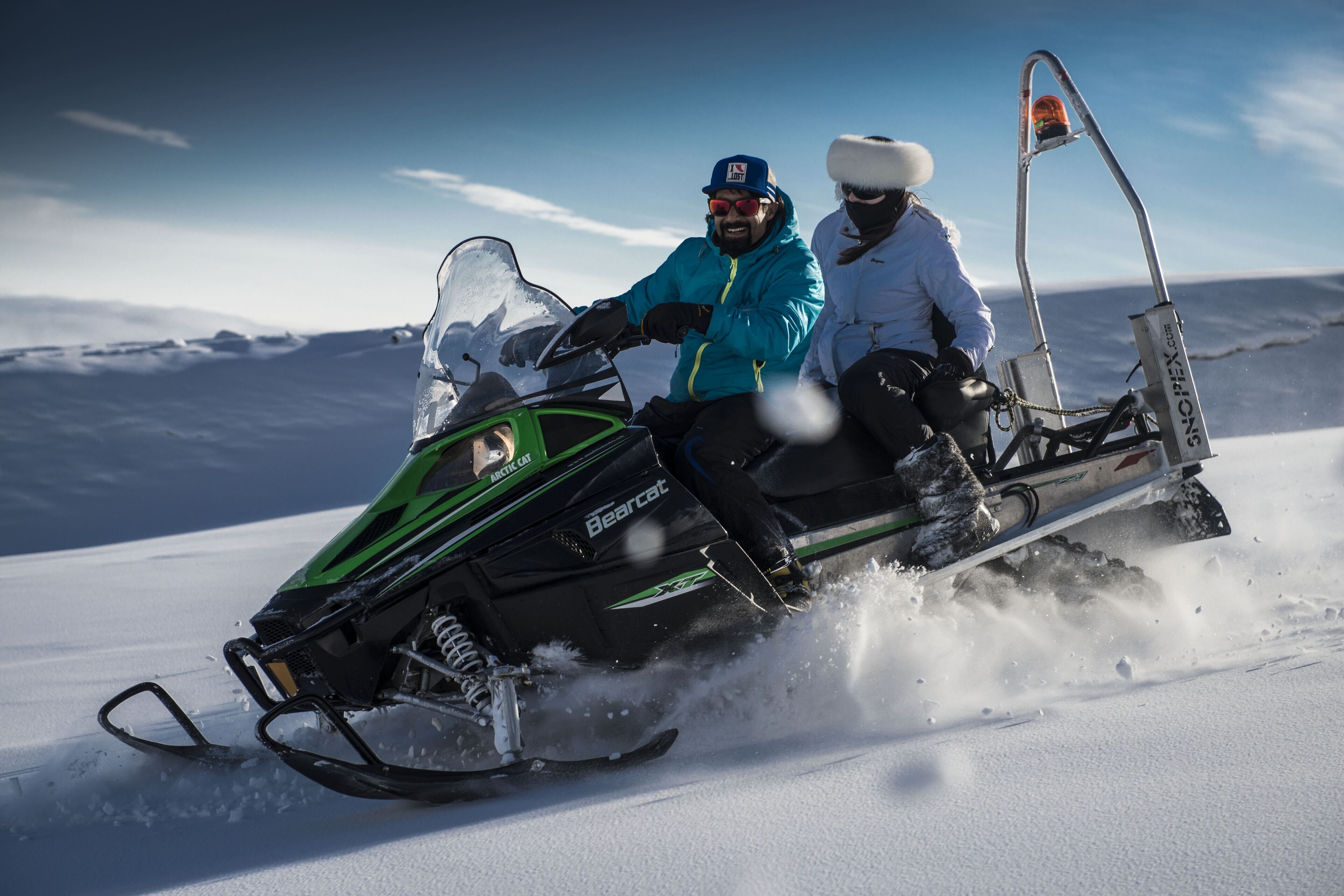 A snowmobile with two people on it, moving on a snowy surface.