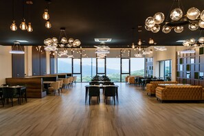 Uma ampla sala de jantar com várias mesas e cadeiras, grandes janelas com vista para as montanhas e iluminação pendente moderna.