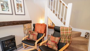 Un salon chaleureux avec deux fauteuils en cuir, un mur en pierre, une cheminée et un escalier.