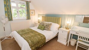 Une chambre à coucher comprenant un lit, des tables de chevet, une commode, une lampe, un ventilateur, une fenêtre avec des rideaux et un radiateur.