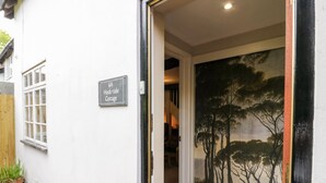 L’entrée d’un chalet est signalée par une plaque indiquant « 6A, Hocktide Cottage ». On y voit une porte avec un panneau de verre et un pot de fleurs placé à l’extérieur.