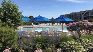 A pool area with blue umbrellas, white lounge chairs, and a clear sky. - Spectacular Montauk Sunset in Gated Community - Perfect for Families! (Montauk)