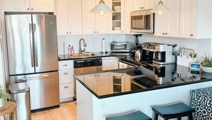 A modern kitchen with white cabinets, stainless steel appliances, and a central island with stools. - Spectacular Montauk Sunset in Gated Community - Perfect for Families! (Montauk)