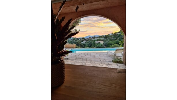 Vue intérieure, prise à travers une porte en arc, donnant sur un espace piscine avec vue sur une colline et des montagnes.