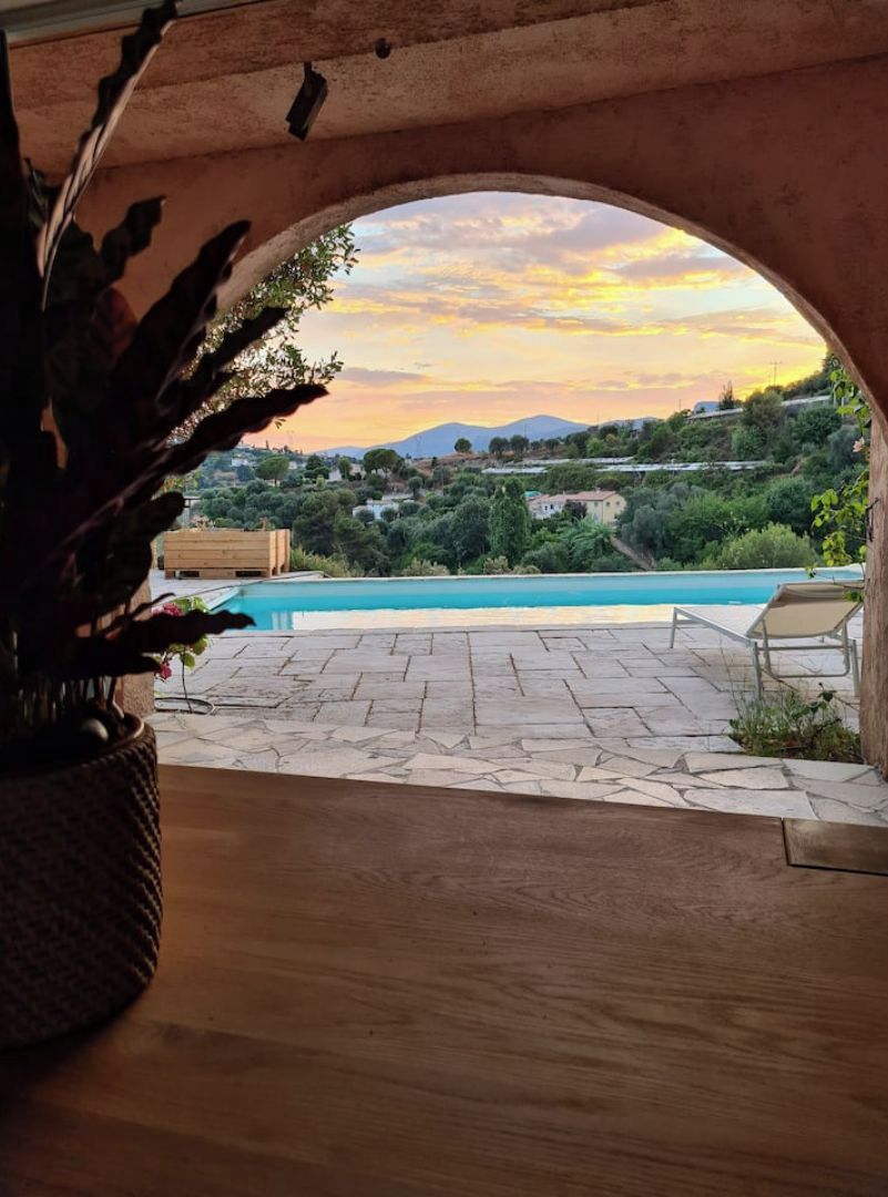 Vista interior a través de un arco que da a una zona de piscina con vistas a una ladera y montañas.