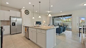 A modern kitchen with white cabinets, a stainless steel refrigerator, and pendant lighting. - Amazing home in Solterra Resort! (Davenport)