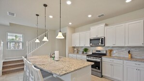 A modern kitchen with white cabinets, granite countertops, stainless steel appliances, and pendant lighting. - Amazing home in Solterra Resort! (Davenport)