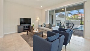 A modern living room with a flat-screen TV, a coffee table, and a sofa. - Amazing home in Solterra Resort! (Davenport)