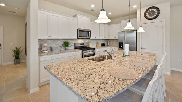 A modern kitchen with white cabinets, granite countertops, stainless steel appliances, and pendant lighting. - Amazing home in Solterra Resort! (Davenport)