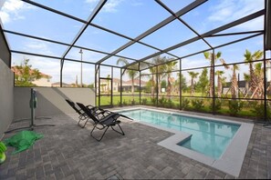 A covered outdoor swimming pool with lounge chairs, a brick floor, and a view of a residential area. - Amazing home in Solterra Resort! (Davenport)