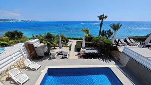 Área de piscina no terraço com vista para o oceano, espreguiçadeiras e guarda-sóis.