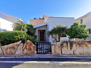 Una casa moderna con entrada protegida por una reja, rodeada de rocas grandes y follaje.