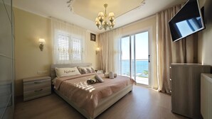 Um quarto espaçoso com uma cama grande, televisão na parede e vista para o mar pela janela.